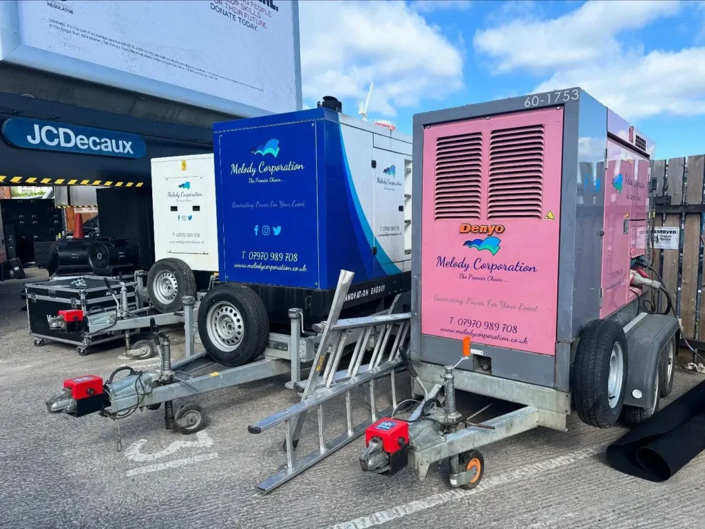 Two trailer-mounted generators, one blue and one pink, are parked side by side in a lot. Both are branded "Melody Corporation" and are secured with wheel locks.